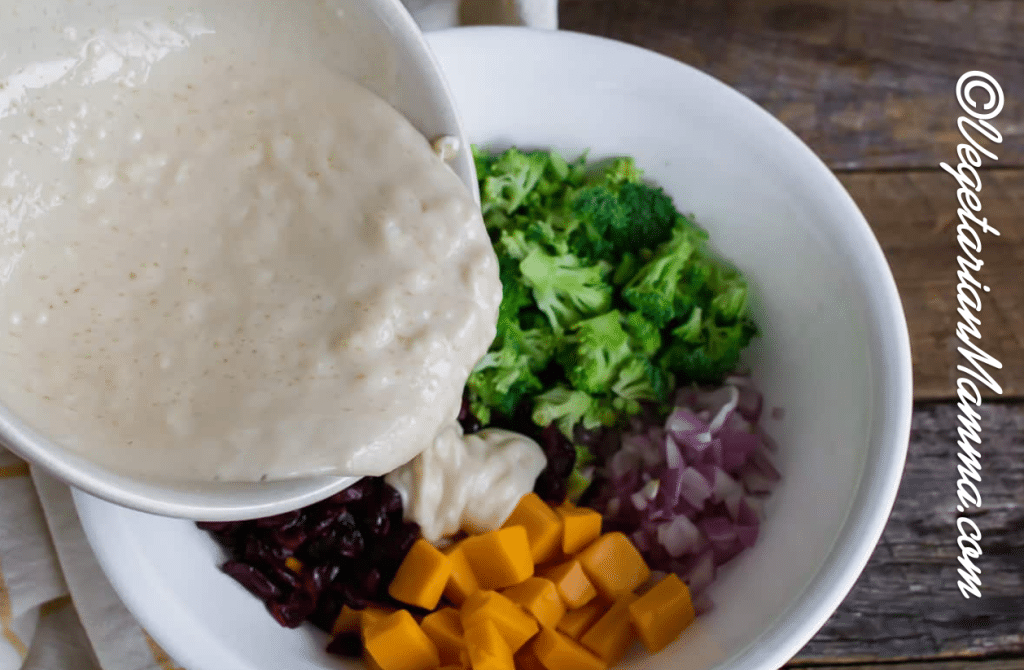 Smaller bowl of dressing being poured onto the veggies and cheese.