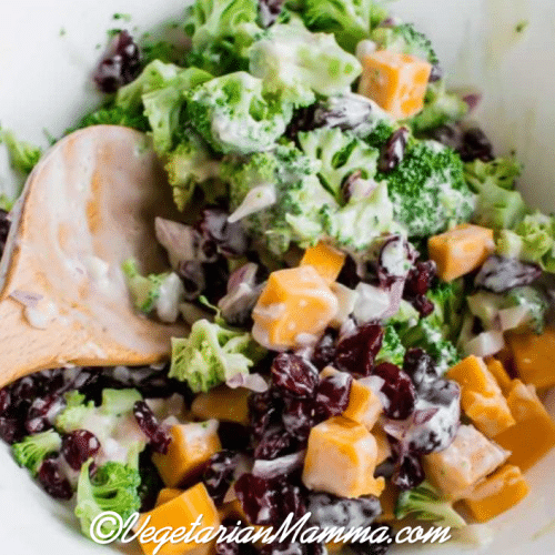 Spoon inside bowl of broccoli salad atop wooden pallet