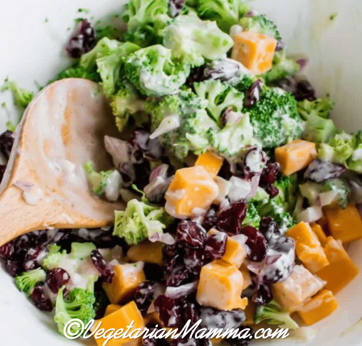 Spoon inside bowl of broccoli salad atop a white bowl.