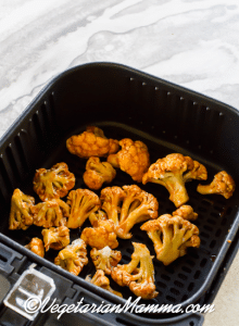 pieces of dipped cauliflower placed in air fryer basket.