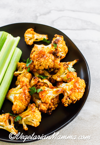 Air Fryer Honey Sriracha Cauliflower is an air fried snack. Cauliflower and celery on a black plate.