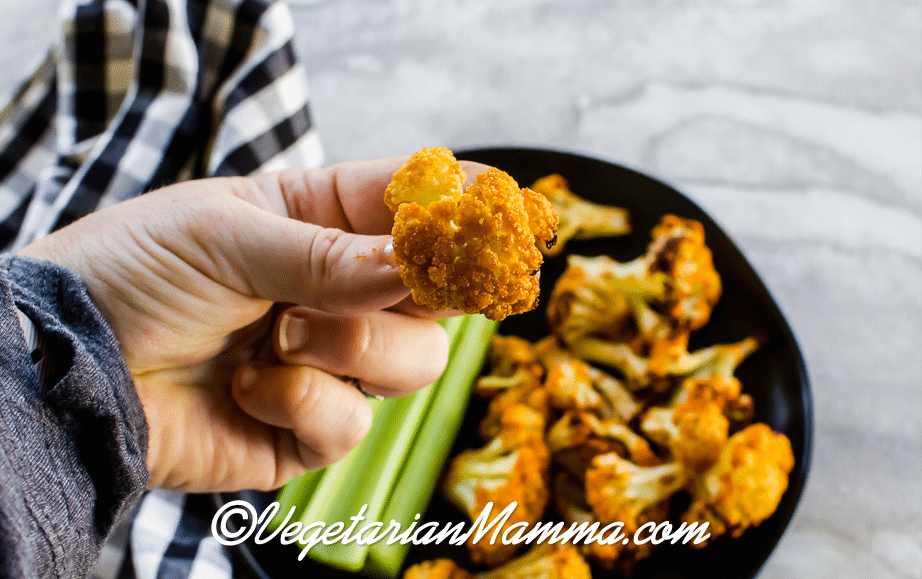 A hand holding a cauliflower covered in siracha sauce.