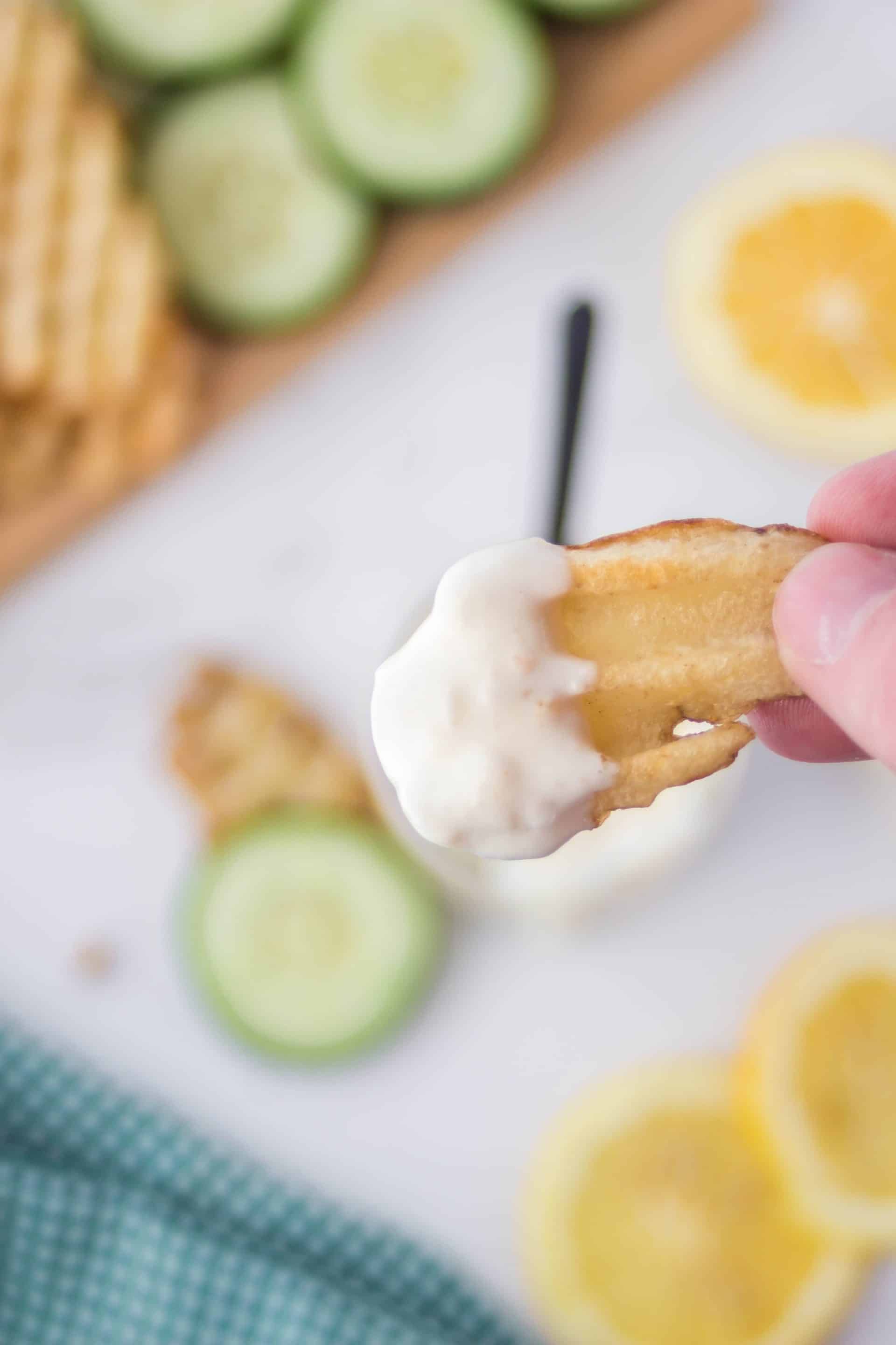 A hand holding a potato chip dipped in lemon aioli over a jar of more sauce