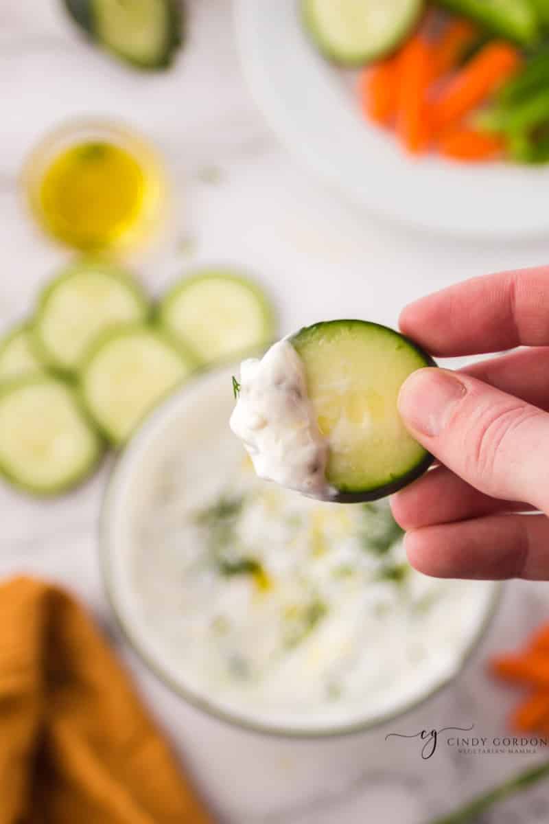 A hand holding a cucumber dipped in creamy mediterranean sauce 