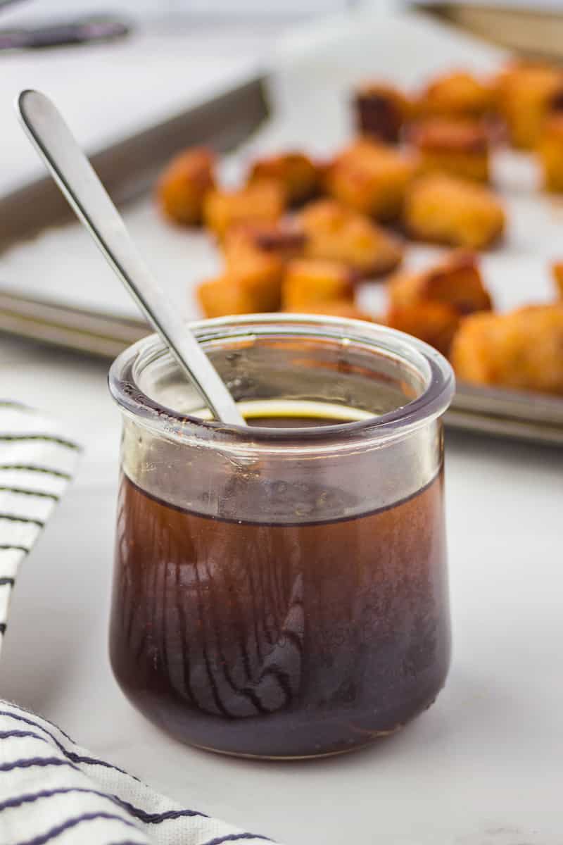 Close-up shot of a clear jar containing a brown marinade with a spoon in it