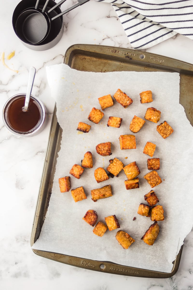 Marinated baked tempeh on parchment paper next to a jar of marinade