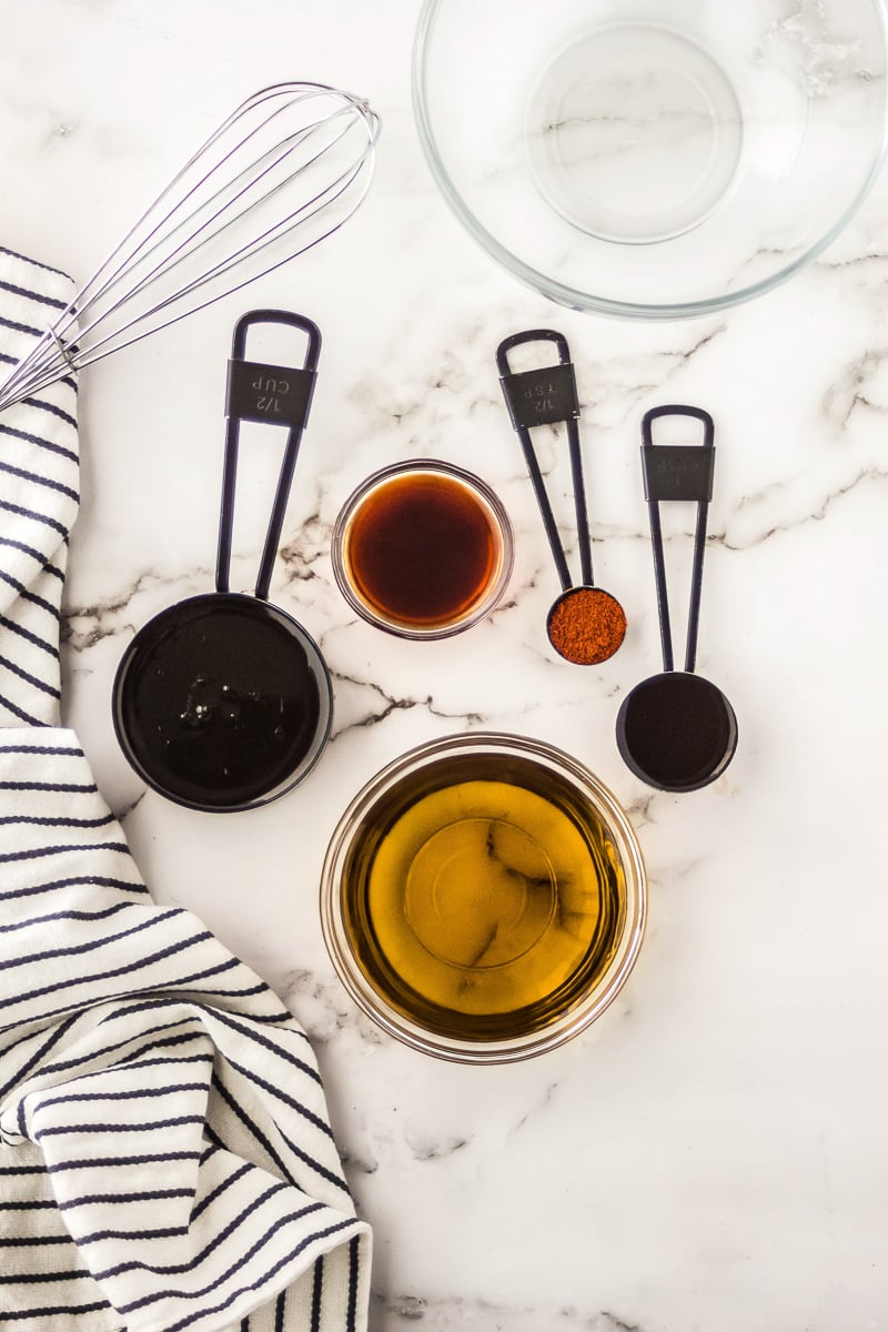 A bowl of oil next to measuring cups of cayenne pepper, Worcestershire sauce, maple syrup, and liquid smoke