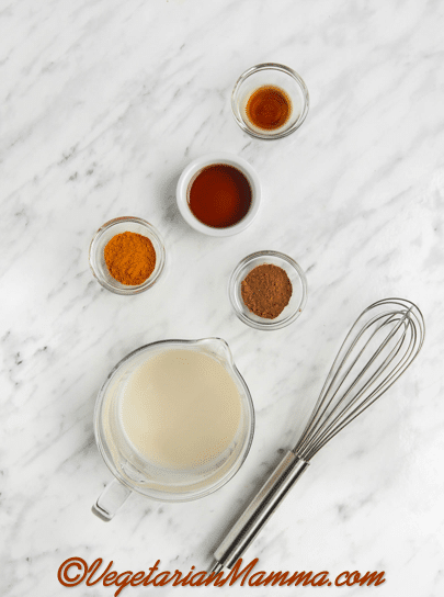 measured ingredients for turmeric latte. Ingredients are in clear and metal containers on a white marble background.