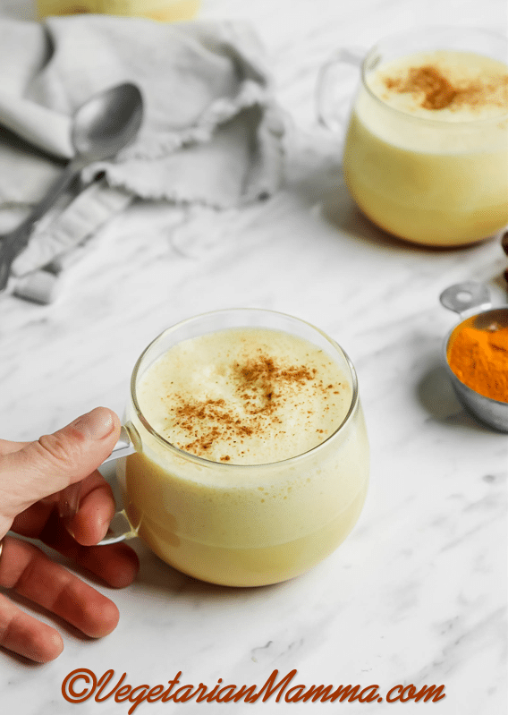 hand coming in from left side holding the clear mug of turmeric coffee