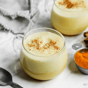 Two cups of turmeric latte in glass mugs with a sprinkle of cinnamon.
