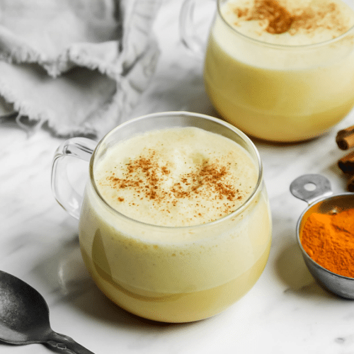 Two cups of turmeric latte in glass mugs with a sprinkle of cinnamon.