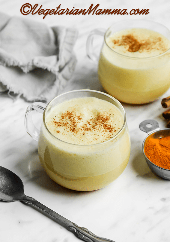 Two cups of turmeric latte in glass mugs with a sprinkle of cinnamon.