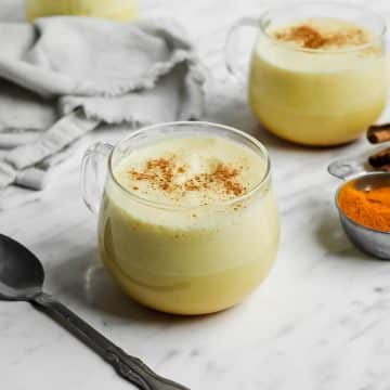 horizontal photo of two clear mugs with pale yellow foamy liquid in them