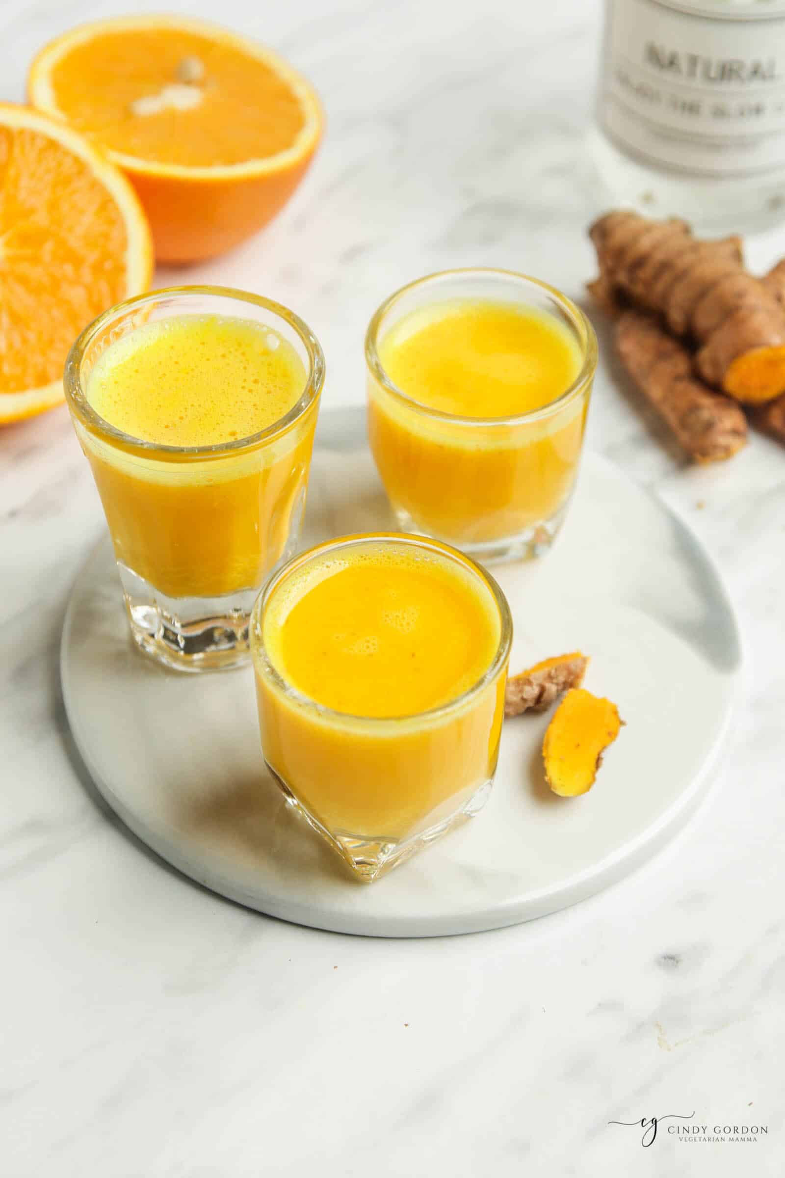 orange cut in half in top left, three clear glasses filled with orang liquid on a white serving tray