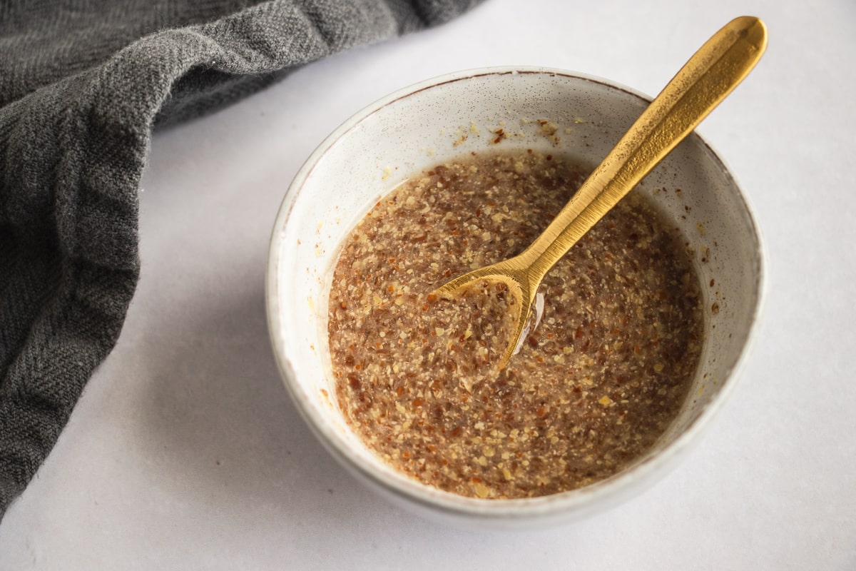 Overhead shot of flaxseed egg in an off-white bowl with a golden spoon 