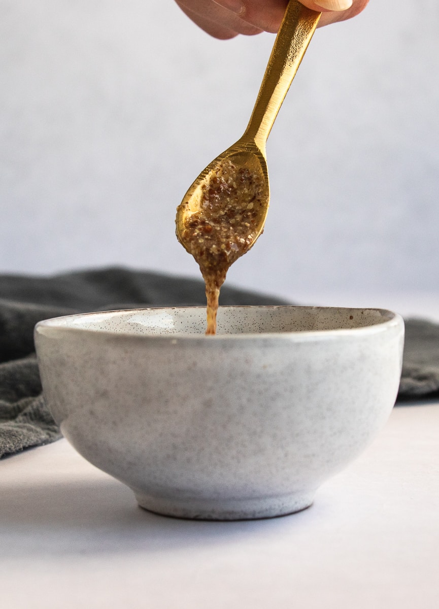 A flax egg dripping off a golden spoon over a ceramic mixing bowl