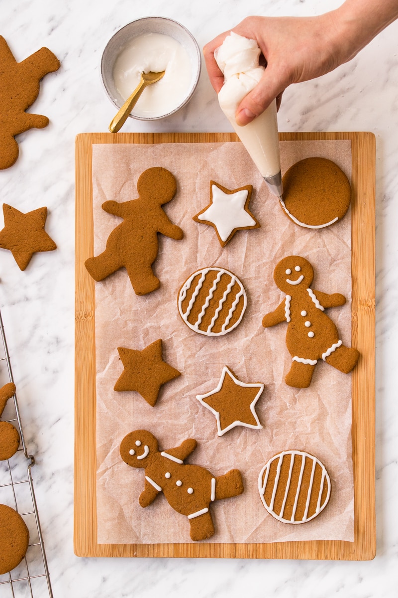 A hand decorating gingerbread cookies with white icing on a cutting board