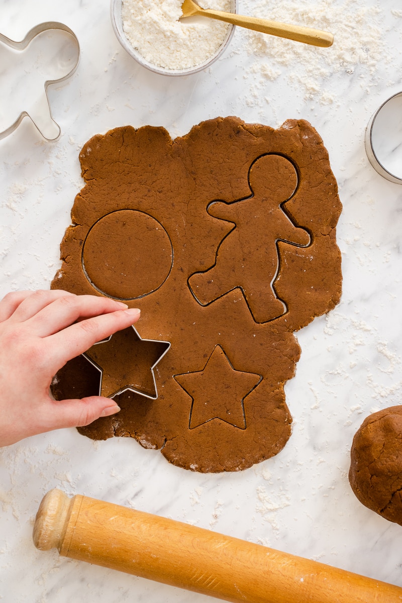 A hand using a star cookie cutter on gingerbread cookie dough