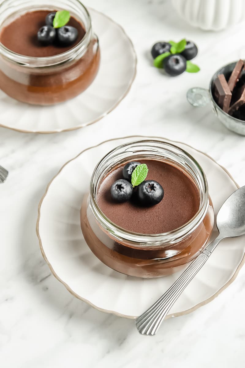 Chocolate panna cotta in a clear glass jar on a white saucer with a silver spoon