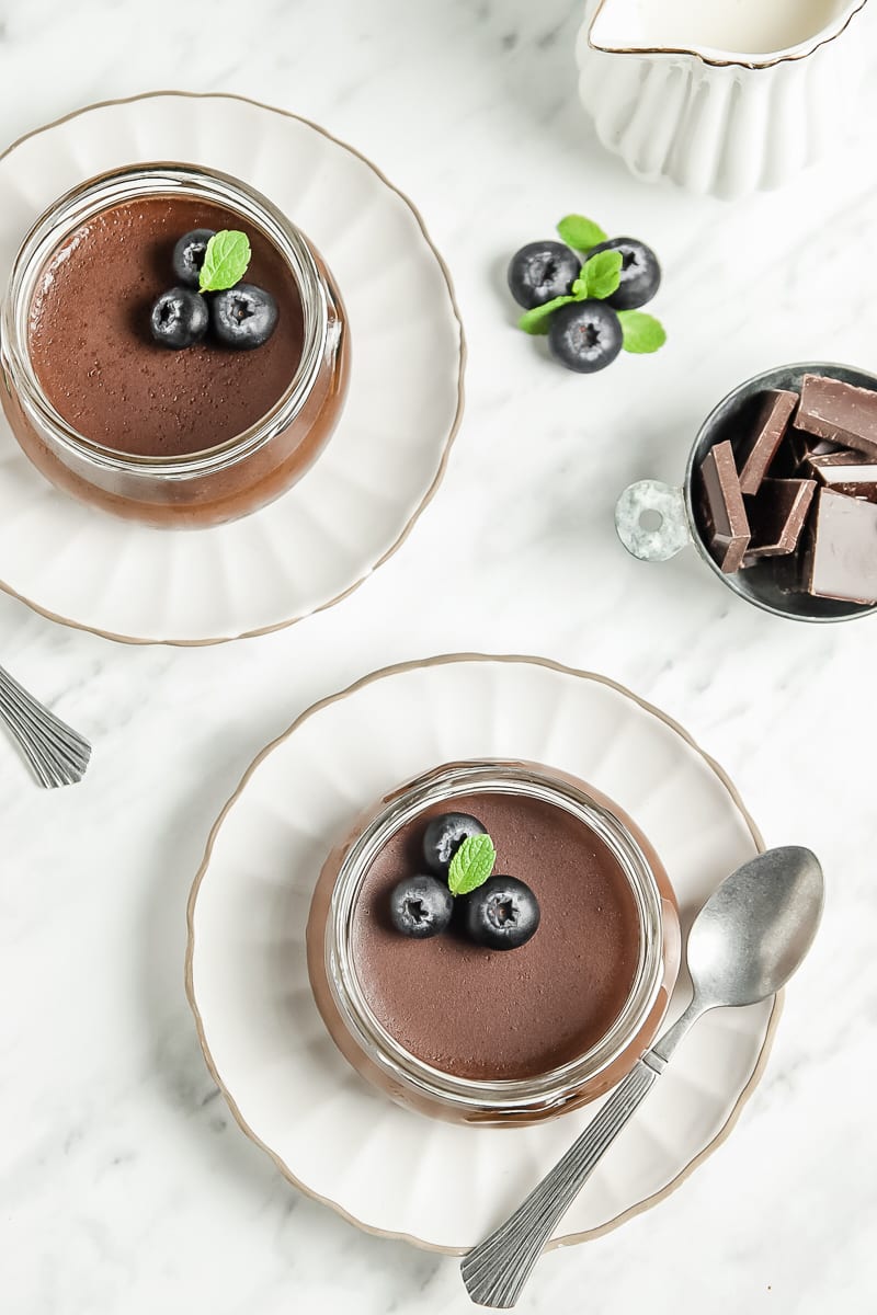 Two clear jars of chocolate panna cotta topped with blueberries and mint