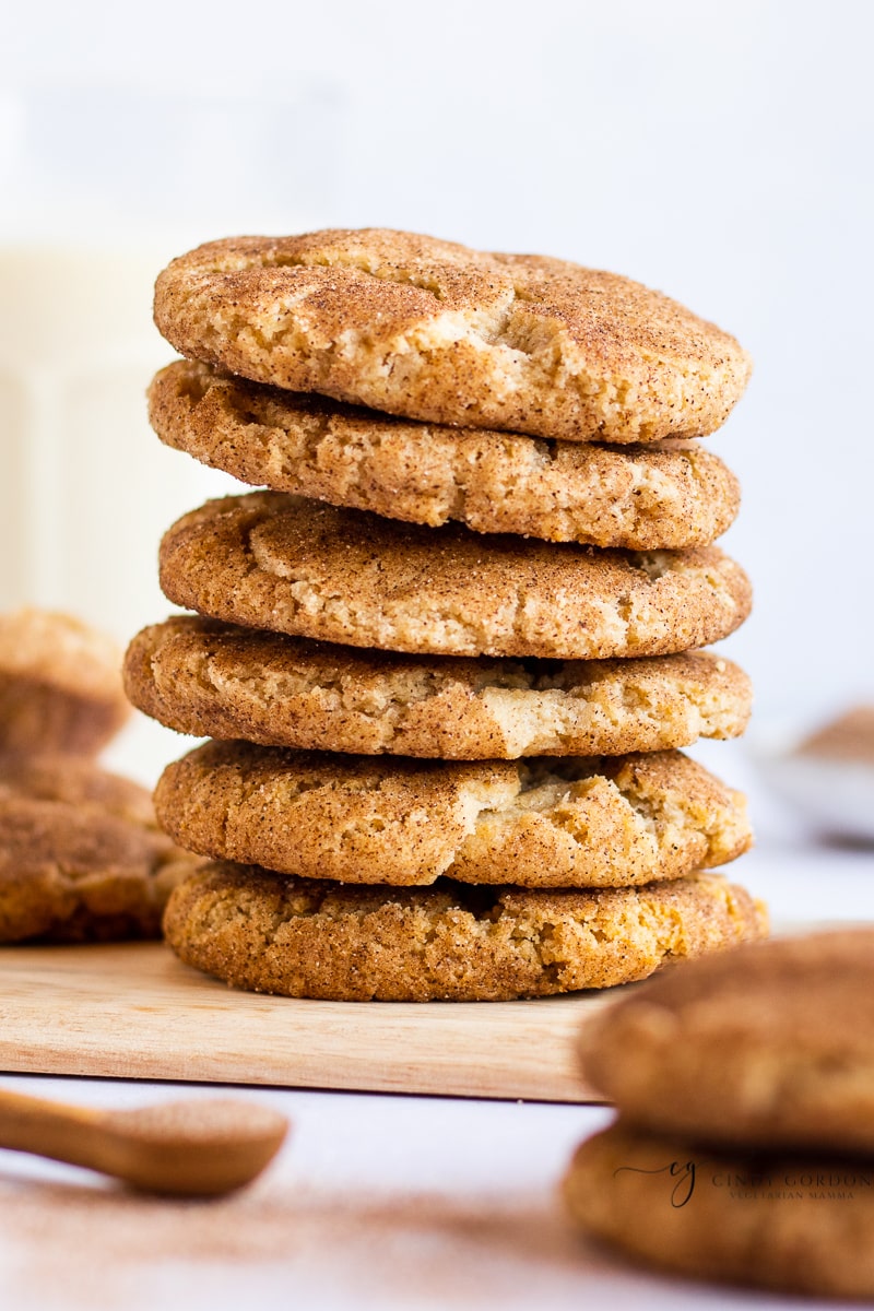 A stack of 6 snickerdoodle cookies on a wooden cutting board surrounded by more cookies