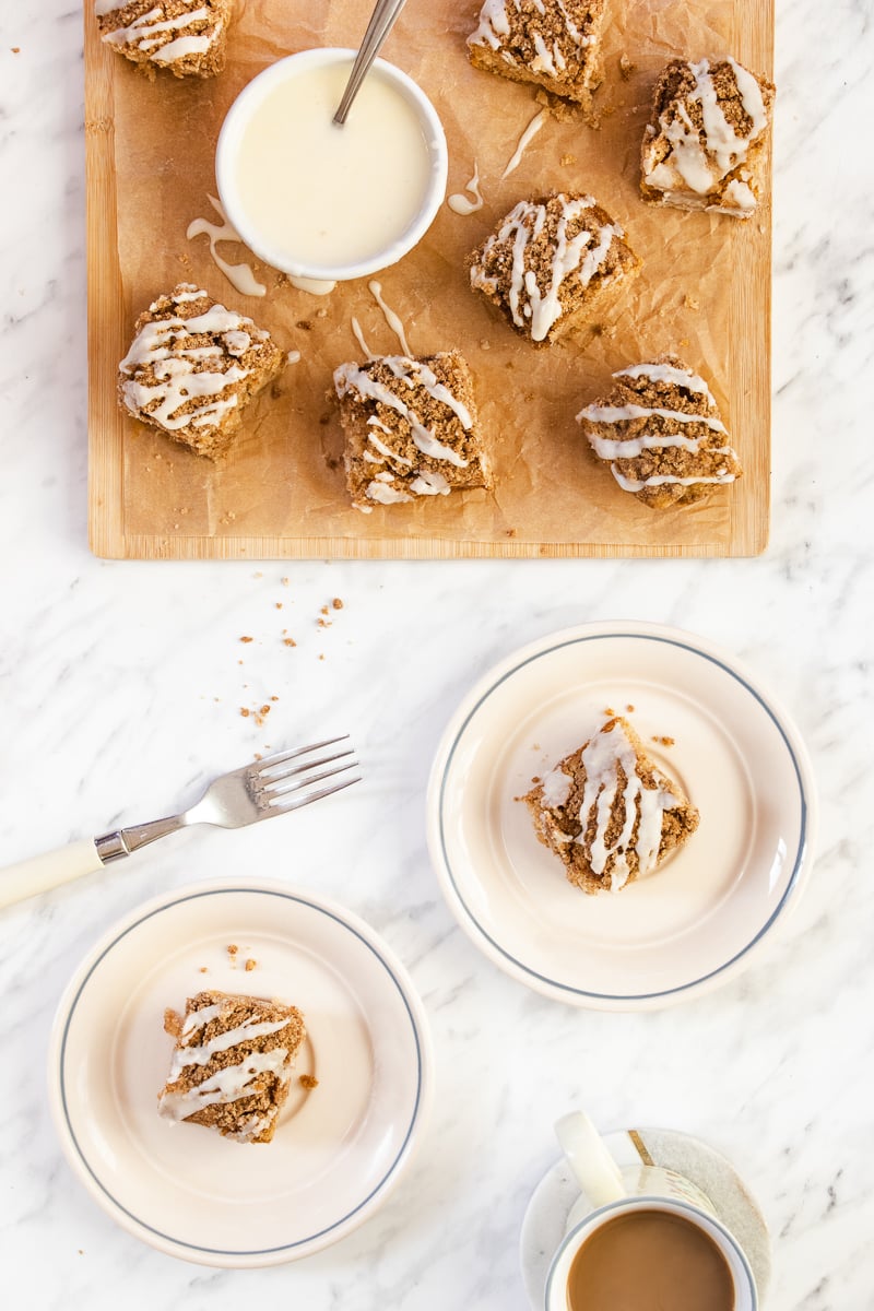 two plates of coffee cake next to a cutting board of more cake with a bowl of icing