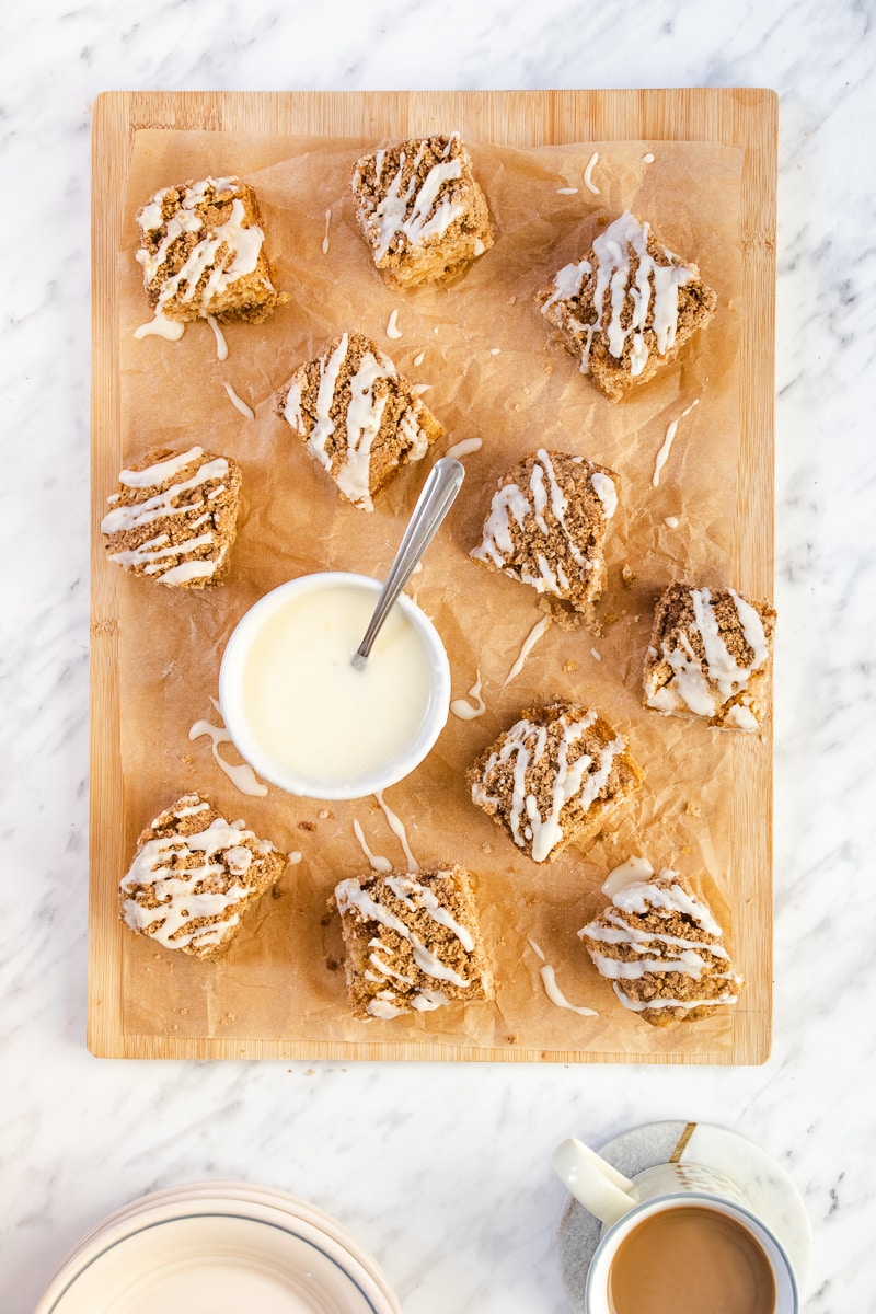 Coffee cake squares on a wooden cutting board with a bowl of white icing