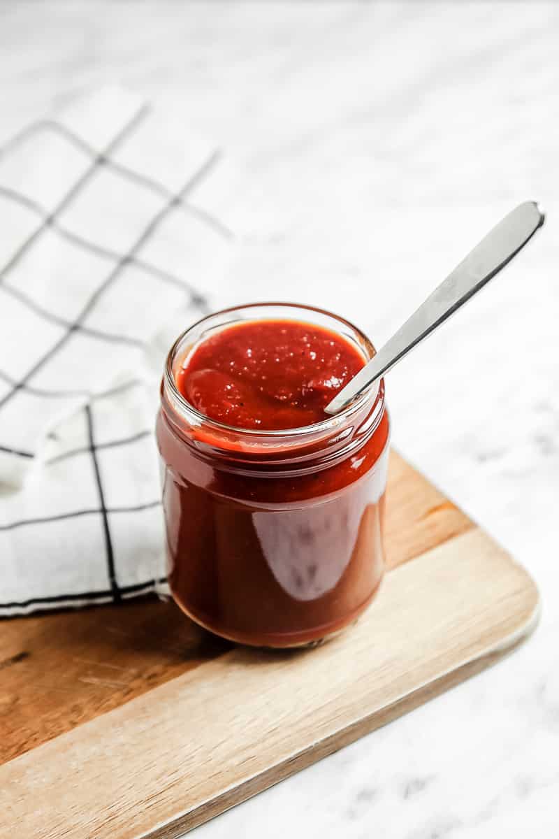 Close-up shot of a jar of vegan bbq sauce with a silver spoon in it