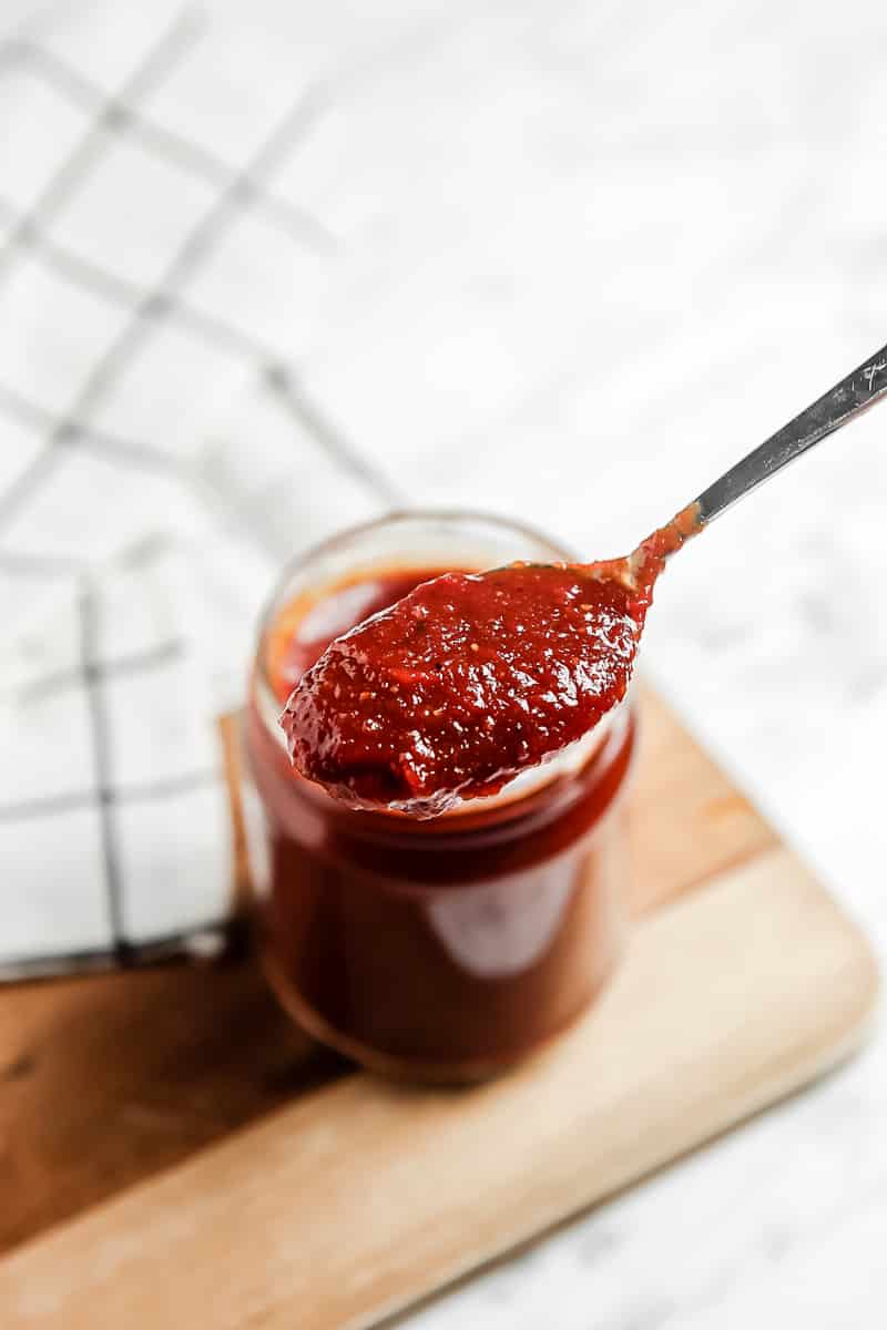 A spoonful of bbq sauce over a jar of more vegan sauce