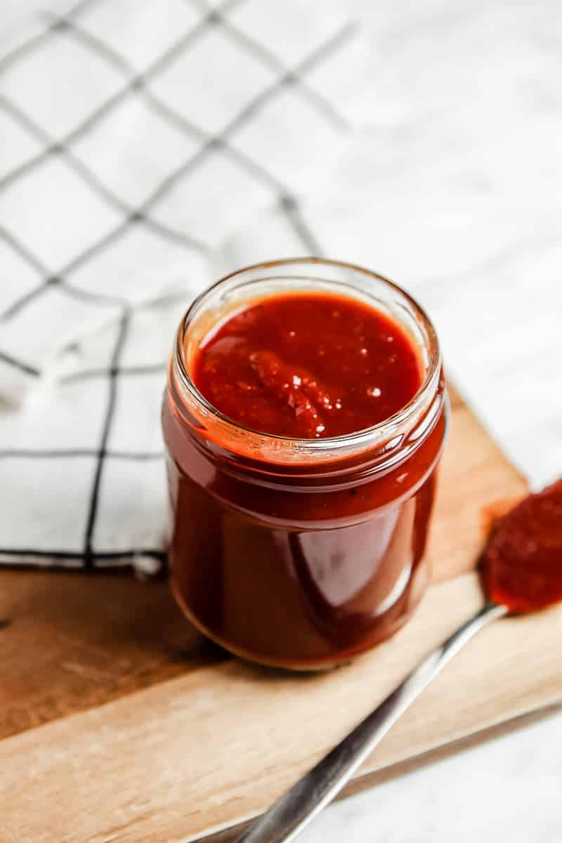 Homemade barbecue sauce in a glass jar next to a spoon covered in sauce