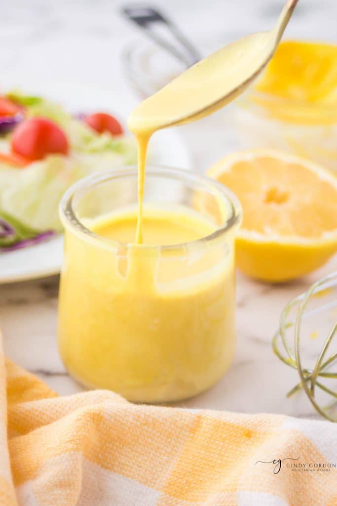 a small glass jar of honey mustard sauce on a marble counter in front of a salad and half a lemon