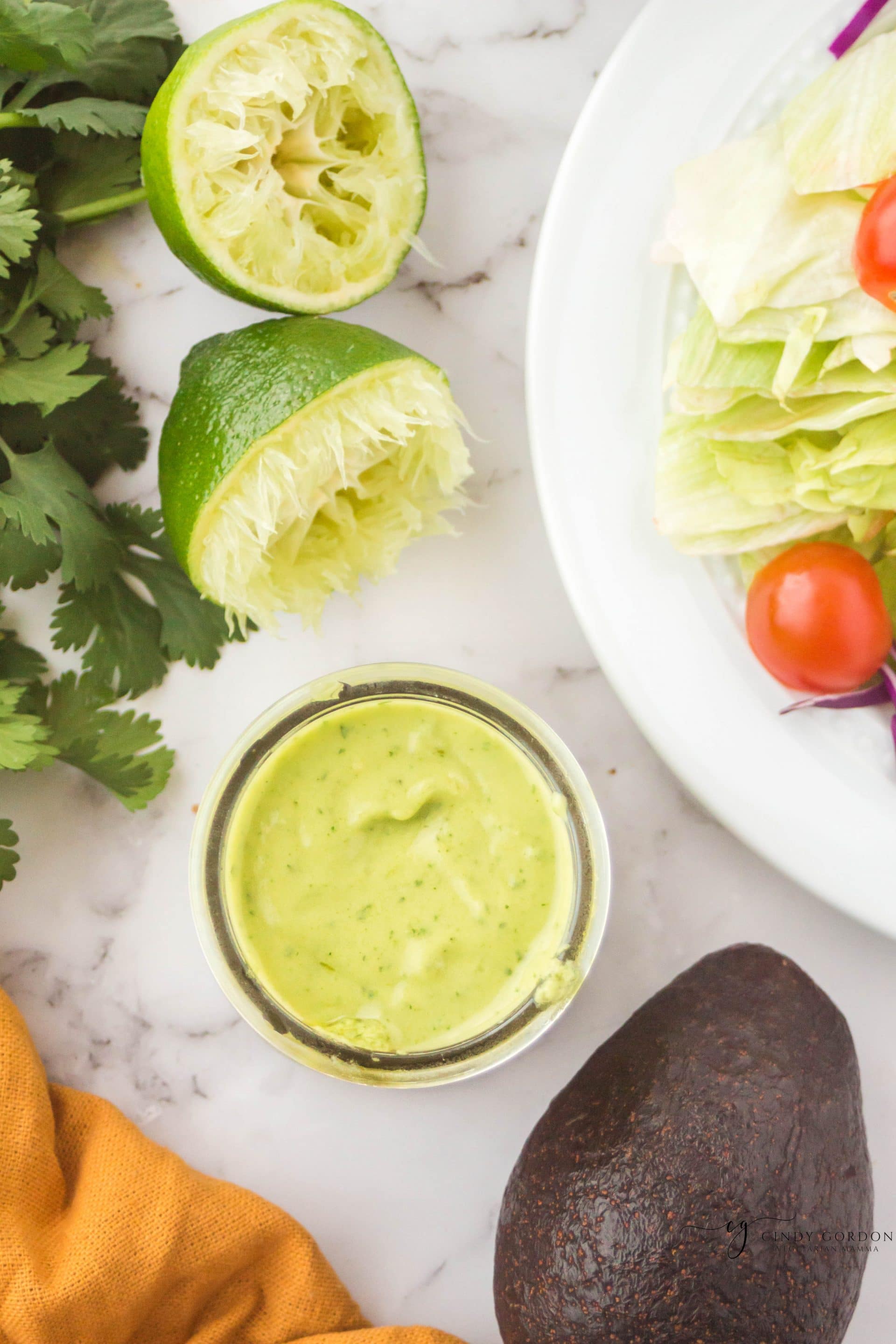 glass jar of green creamy liquid next to an avocado and an orange napkin