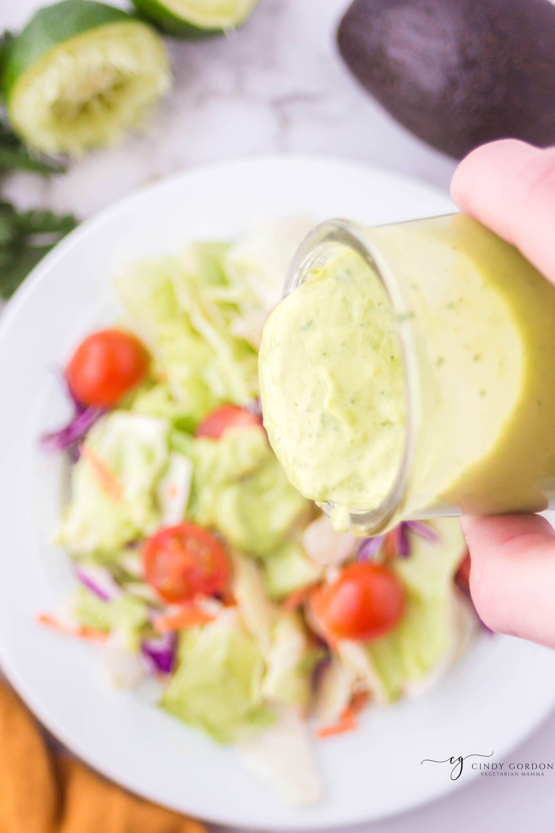 a salad of lettuce and tomatoes with avocado dressing being poured on