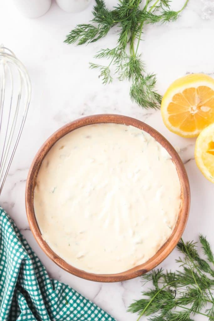 brown wooden bowl filled with creamy white sauce. cut lemons to trop right, whisk to left