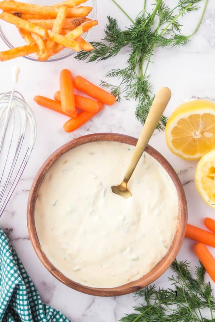 brown bowl filled with off white sauce, golden spoon in bowl carrots, cut lemon and dill to the right side