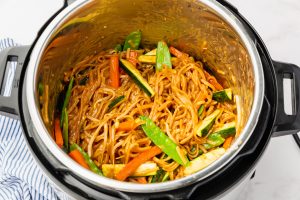 instant pot with cooked noodles with brown sauce and carrots, snow peas and zucchini