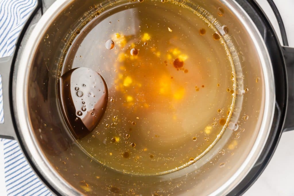 Instant Pot with vegetable stock, soy sauce, brown sugar, sesame oil, lime juice, garlic, and ginger.
