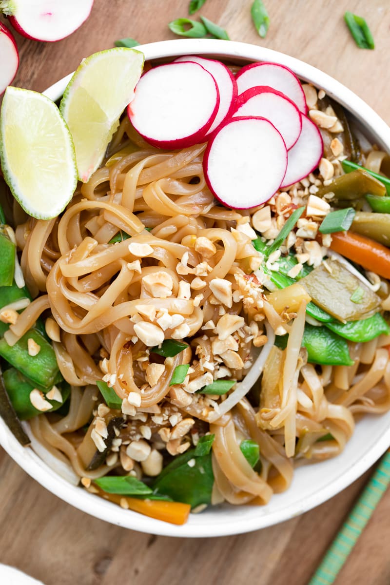 Overhead shot of instant pot pad Thai garnished with vegetables, lime wedges, and peanuts