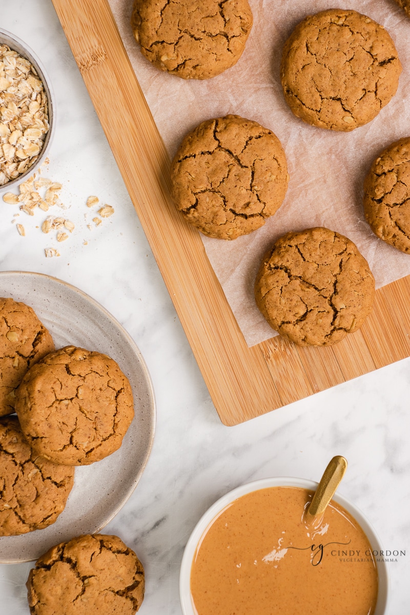 Vegan peanut butter oatmeal cookies on a cutting board and on a plate next to a bowl of peanut butter