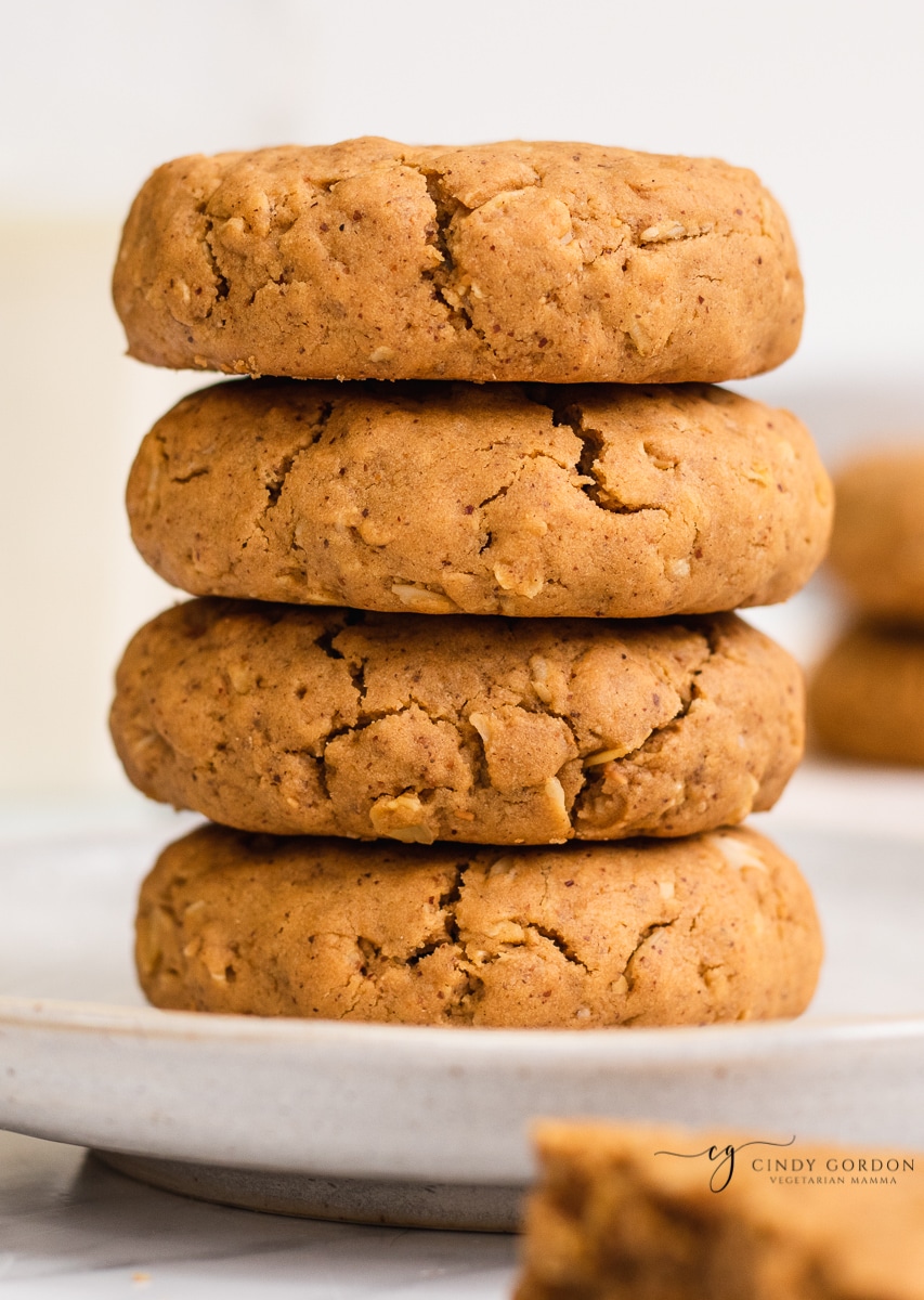 A stack of 4 vegan peanut butter cookies with rolled oats on a cream plate 