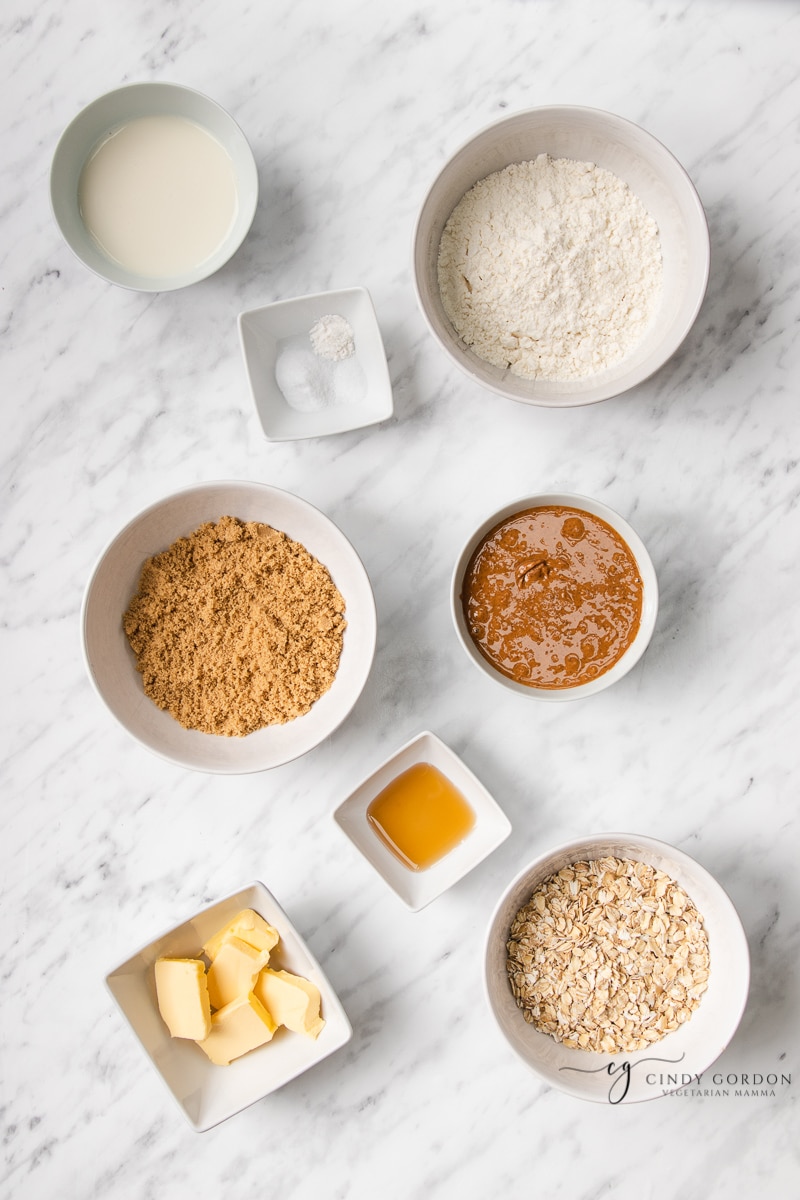 Bowls of gluten-free flour, peanut butter, brown sugar, vanilla extract, almond milk, salt, vegan butter, and rolled oats