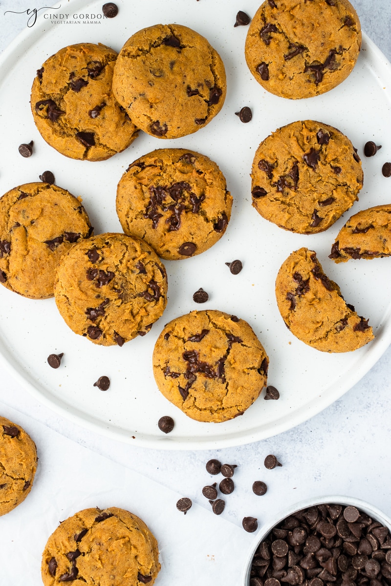 Vegan pumpkin chocolate chip cookies on a white plate surrounded by chocolate chips