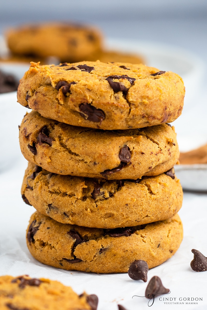 A stack of vegan pumpkin chocolate chip cookies surrounded by dark chocolate chips