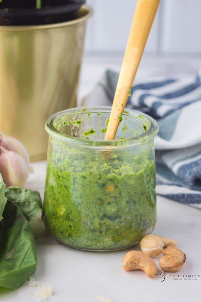 a small jar filled with green cashew pesto with a gold spoon in it