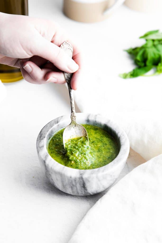 a hand stirring a bowl of pesto with a spoon 