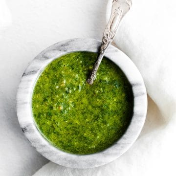 a marble bowl filled with green basil pesto with a silver spoon in it