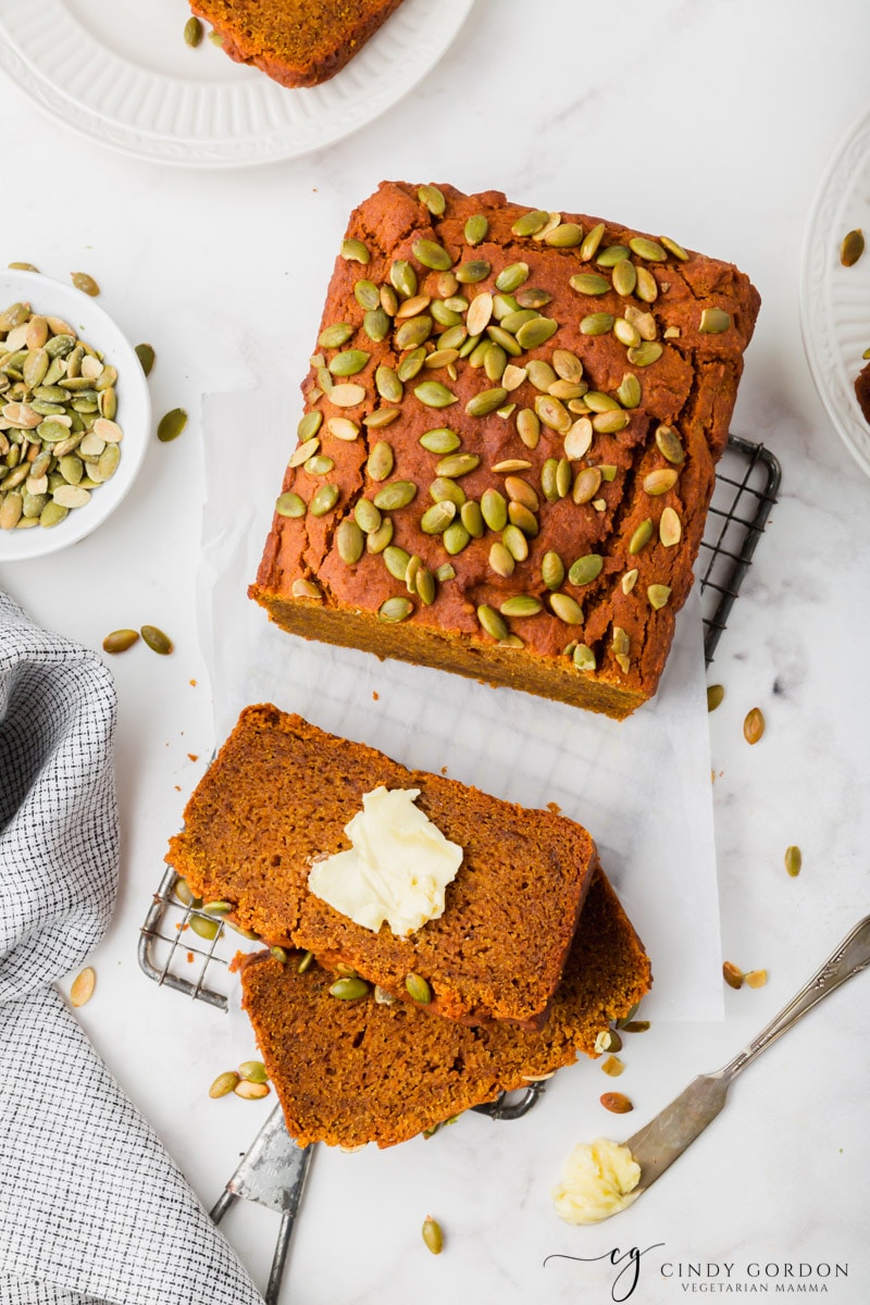 Slices of pumpkin bread with butter next to a loaf of bread garnished with pumpkin seeds