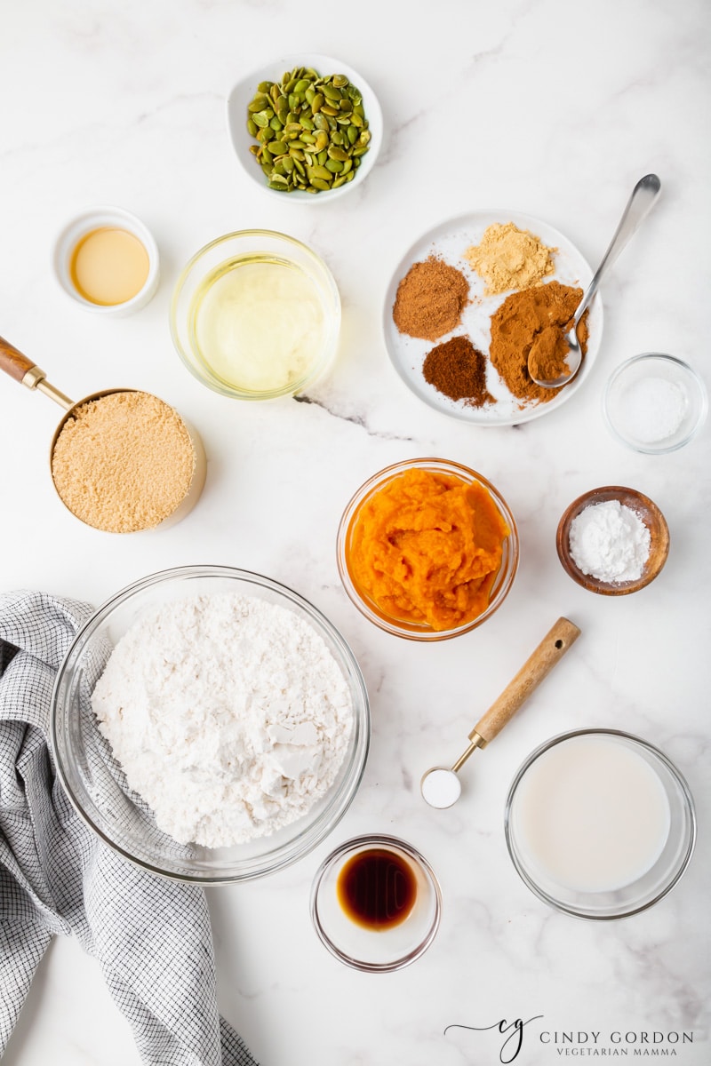 Bowls of flour, pumpkin puree, pumpkin pie spices, baking powder, baking soda, brown sugar, and vegetable oil