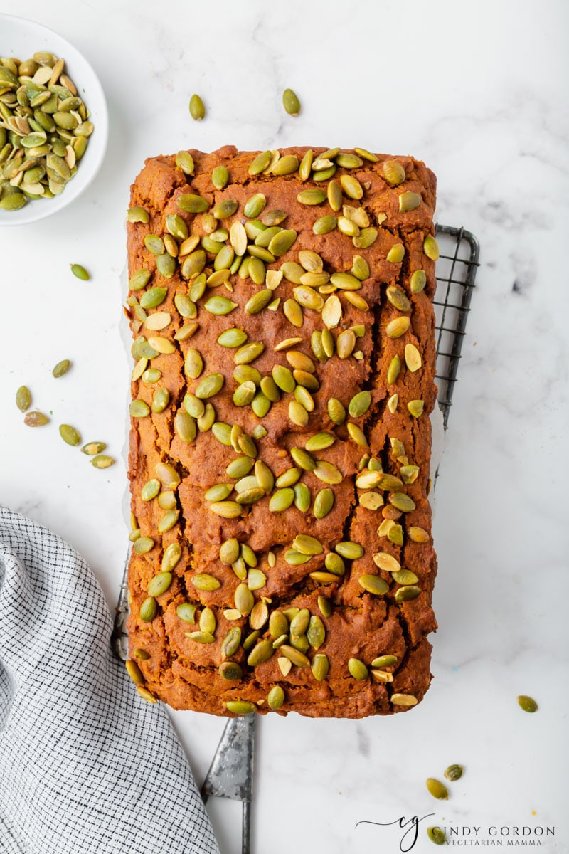 Overhead shot of a loaf of pumpkin bread garnished with seeds on a wire cooling rack