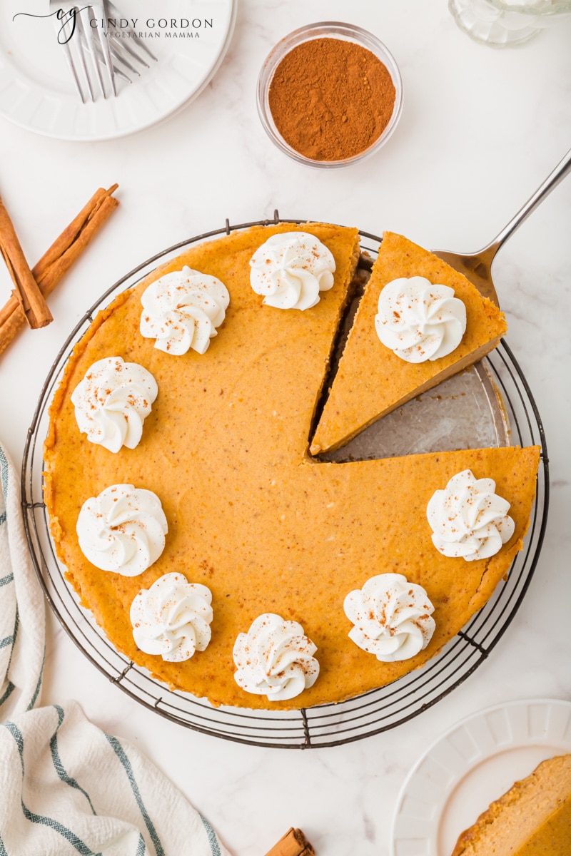 Overhead shot of a vegan pumpkin cheesecake with a cut slice on a spatula